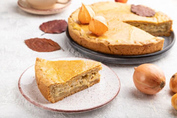 Autumn onion pie decorated with leaves and cup of coffee on gray concrete background. Side view.