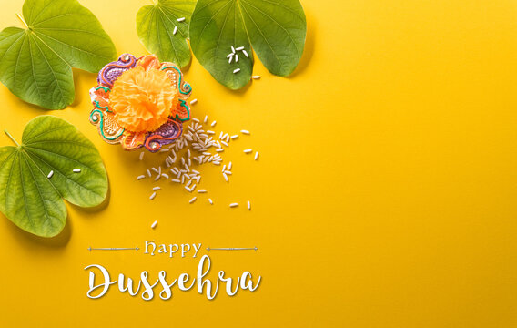Happy Dussehra. Yellow flowers, green leaf and rice on yellow paper background. Dussehra Indian Festival concept.