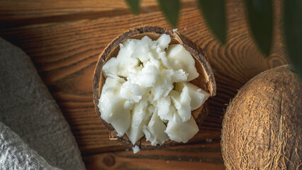 Pieces of organic coconut butter in a bowl and fresh coconut on a wooden table. Concept of healthy ingredient for cooking and natural cosmetics