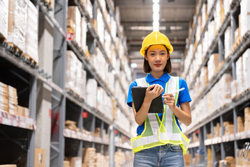 Beautiful asian engineer woman wearing safety helmet and reflective vest, She checking goods supplies on shelves with tablet in ware house and looking camera. Logistic and business export concept.	