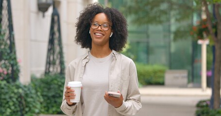 Good looking positive woman walking with coffee and having a phone call in the urban city, enjoying her conversation