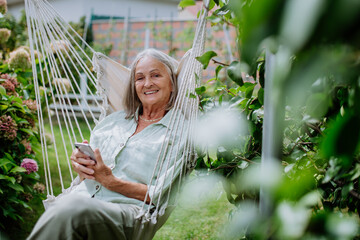 Senior woman relaxing in garden swing with smartphone.