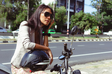 Fototapeta na wymiar Transgender person with sunglasses sitting on motorbike doing her hair looking at mirror on sunny day. Thai woman holding helmet getting ready for ride