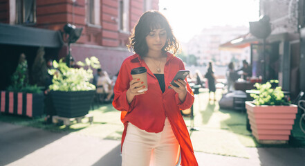 Young woman with smartphone and coffee standing on street