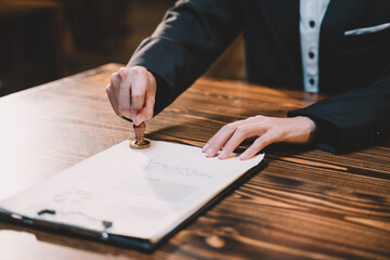 A seal to show approval of an agreement or contract by an authorized person. A businesswoman is about to stamp a document at the office legally. The boss signs the certificate or letter on the desk.