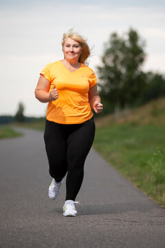 Overweight European middle-aged woman in tracksuit jogging, playing sports.