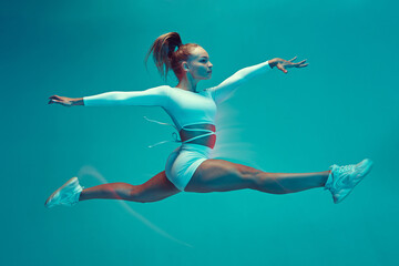 A beautiful girl in a white sports uniform does the splits in a jump. Dancing, sports, grace, stretching.