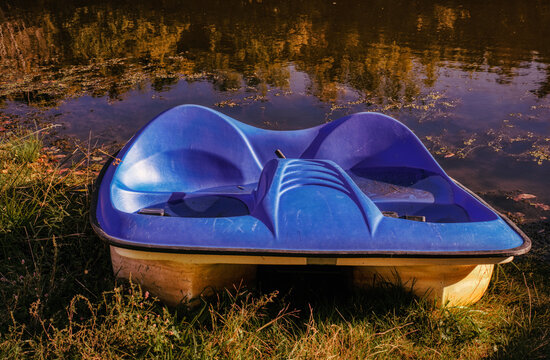 A blue and white 2-person padel boat sits on the shore of a pond as the sun sets on a beautiful September Day in Upstate NY.