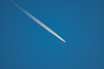 A plane can be barely seen but the vapor trail leaving the twin engines is bright white against the clear blue sky.  
