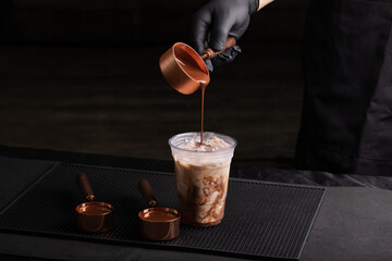 Liquid chocolate or cocoa in a measuring spoon is poured into a glass with milk.