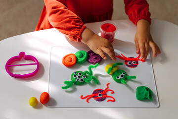 Child hands creating playdough funny monsters for the holiday of Halloween. Sensory play for...