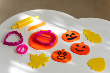 Funny and angry pumpkins and autumn leaves made from plasticine for the holiday of Halloween on the table. Sensory play for toddlers. Holiday Art Activity for Kids.