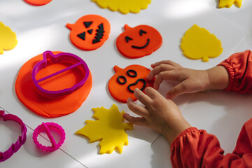 Child hands creating playdough funny and angry pumpkins and autumn leaves for the holiday of Halloween. Sensory play for toddlers. Holiday Art Activity for Kids.