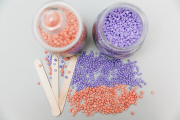 Close-up of lilac and pink wax granules scattered from a jar. Cosmetic procedure to remove unwanted hair from the body. depilation and epilation.