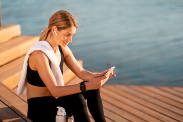 Fototapeta na wymiar Middle Aged Athletic Woman Resting With Smartphone After Outdoor Workout
