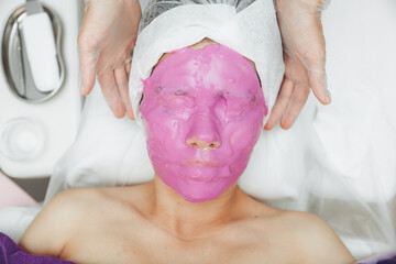 Care for the beauty of women's skin. A young woman with an alginate cosmetic purple mask on her...