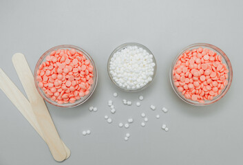 Beautiful granules of pink, white, yellow, blue wax for depilation in a glass bowl, wooden spatulas...