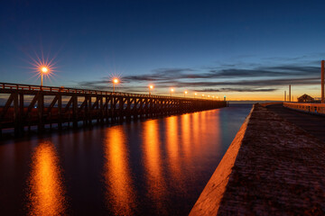 Fototapeta na wymiar Hafenausfahrt Blankenberge zum Meer mit einer langen Holzbrücke und beleuchteten Laternen in der Abenddämmerung 
