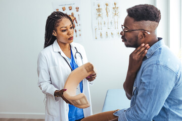 Female physiotherapist or traumatologist examines a male patient sitting in the neck collar. Doctor explains the diagnosis to the male patient and tells about the duration 