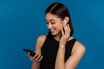 Asian young woman in earphones smiling while using mobile phone