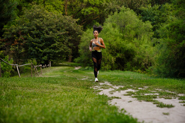 Fototapeta premium Young black woman in sports wear running at summer park