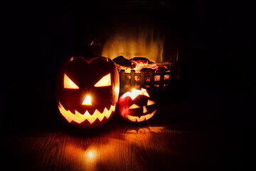 Two Jack-o'-lantern pumpkins near burning fireplace in the dark