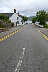 Fototapeta na wymiar Empty road with yellow and white paint lane markings with a pavement and a house wall in Ullapool, Highland, Scotland