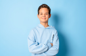 Happy young caucasian boy in casual outfit with arms crossed isolated over blue background © Danko
