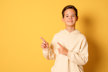 Portrait of cheerful boy pointing to the side - isolated over yellow background. 12 year old kid pointing something. Child points by fingers to the side, at studio