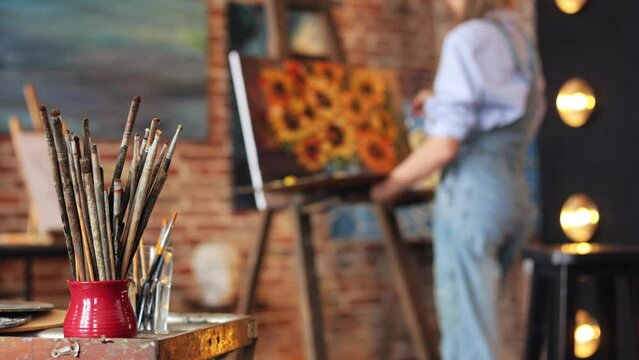 Working process in art studio. Set of painting brushes and palette. Painter creating still life with sunflower on canvas using oil paintings and palette knife. Creative process, relax, leisure, hobby.