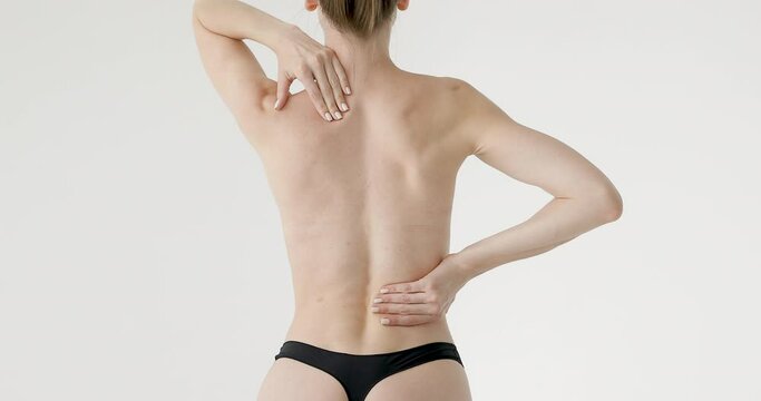 Topless young woman touches and rubs her back. Back problems. Back pain. Girl on a white isolated background