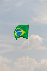 Bandeira do Brasil voando e tremulando ao vento com céu nublado ao fundo.
