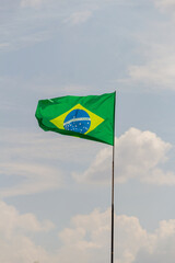 Bandeira do Brasil voando e tremulando ao vento com céu nublado ao fundo.