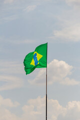 Bandeira do Brasil voando e tremulando ao vento com o céu nublado ao fundo.