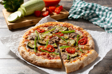 Vegetarian pizza with zucchini, tomato, peppers and mushrooms on wooden table