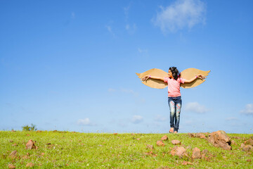 happy excited girl kid with artificial wings dancing like a bird on top hill in green meadow against blue sky - concept of freedom, happines and independence