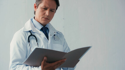 pensive doctor in white coat reading documents in folder on grey background.