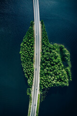 Aerial view of road through blue lakes or sea with green woods in Finland.