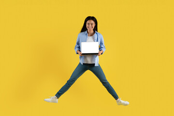 Smiling young chinese woman student in casual jumping, showing laptop with blank screen