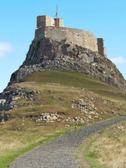 Lindisfarne Castle atop its dramatic, commanding outcrop in bright sunlight, looking every inch a mythic, legendary stronghold.