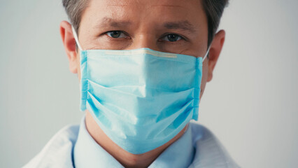 portrait of doctor in medical mask looking at camera isolated on grey.