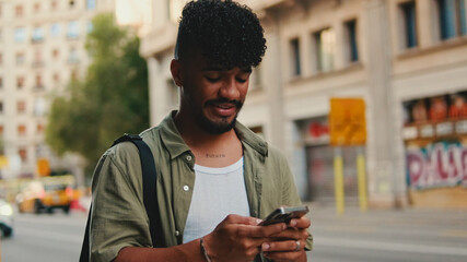 Young smiling man with beard dressed in an olive color shirt uses phone map app on the old city background