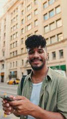 Young smiling man with beard dressed in an olive color shirt uses phone map app on the old city background