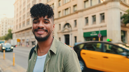 Close up, young happy man with beard dressed in an olive color shirt stands next to the road
