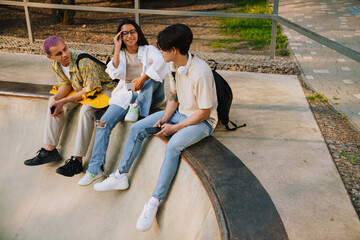 Three young stylish friends sitting on skatepark pool