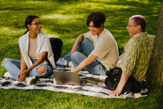Three friedns sitting on a mat on grass in park