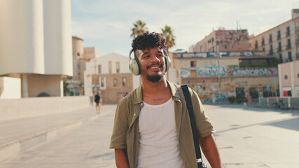 Young man with beard in an olive-colored shirt listens to music on headphones, dances