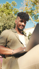 Close up, young male student wearing an olive colored shirt is working on pc laptop while sitting on bench outside the university © Andrii Nekrasov