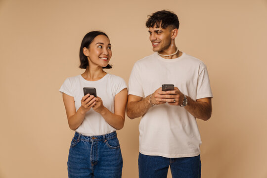 Young Multiracial Couple Smiling And Using Mobile Phones