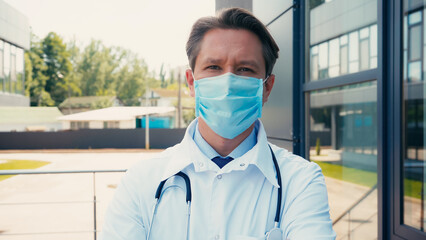 Fototapeta na wymiar doctor in white coat with medical mask and stethoscope looking at camera outdoors.